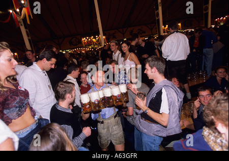A man wearing lederhosen carrying several steins of beer at the Oktoberfest, Munich, Germany Stock Photo
