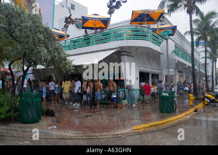 people sheltering from a rainstorm on the pavement outside a bar on Ocean Drive in South Beach Miami Florida USA