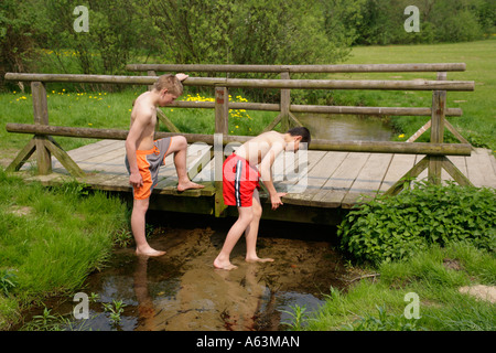 two young boys playing in a stream beside a wooden bridge Stock Photo
