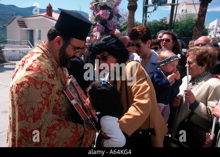 A mother lifts her little girl to kiss the Holy Bible on Easter Day during Easter celebrations on Andros Island Stock Photo