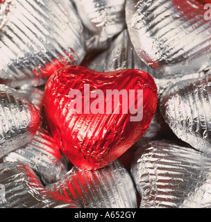 A single wrapped chocolate heart in red foil on silver hearts. Stock Photo