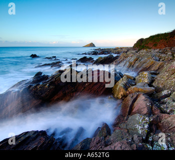 Beautiful dawn light at Wembury Beach with the sea cascading over the exposed rocks and the Mew Stone on the horizon Stock Photo