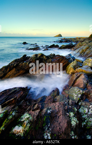 Beautiful dawn light at Wembury Beach with the sea cascading over the exposed rocks and the Mew Stone on the horizon Stock Photo