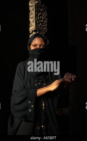 Swahili woman wearing a traditional bui bui standing in a Zanzibar doorway Zanzibar Tanzania Stock Photo