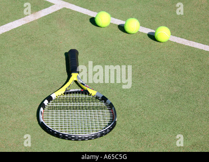 Three green tennis balls and racket on sunny tennis court, high angle view Stock Photo