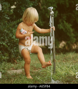 small boy rinsing foot under outdoor faucet Stock Photo