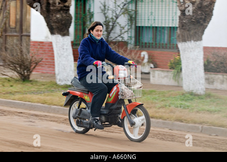 Young Woman Riding Motor Scooter Down Dirt Road in Small Village Lincoln Buenos Aires Argentina Stock Photo