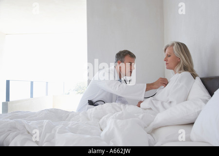 Doctor doing house call on mature woman in bed, using stethoscope, side view Stock Photo