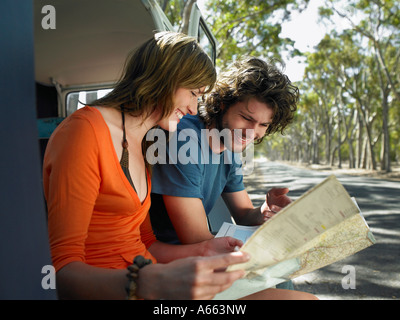 Young couple looking at map, sitting in open camper van at side of road Stock Photo
