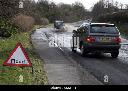 Triangular warning sign by vehicles driving, splashing & waiting to drive, through deep flood water blocking road - near Otley, West Yorkshire, UK. Stock Photo