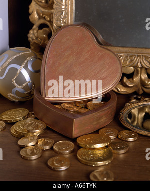 Foil-covered chocolate coins and heart-shaped wooden box in front of gilt mirror frame Stock Photo