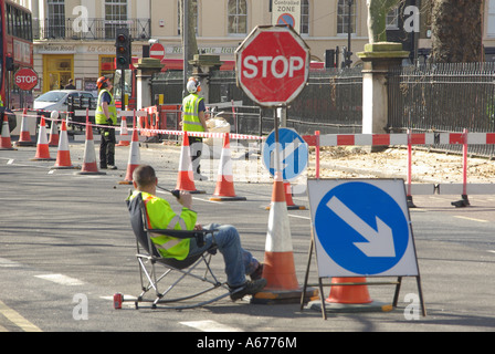 London sitting down on the job concept ideas image workman seated controlling traffic around road works with stop go board Stock Photo