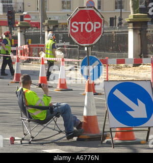 London sitting down on the job concept ideas image workman seated controlling traffic around road works with stop go board Stock Photo