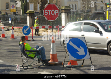 London sitting down on the job concept ideas image workman seated controlling traffic around road works with stop go board Stock Photo