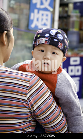 CHINA BEIJING Young Chinese mother carries her inquisitive infant son on the sidewalk in front of the shops where she works Stock Photo
