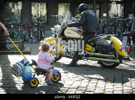 contrast, toddler on toy motorcycle and impressive leather clad bike rider Stock Photo