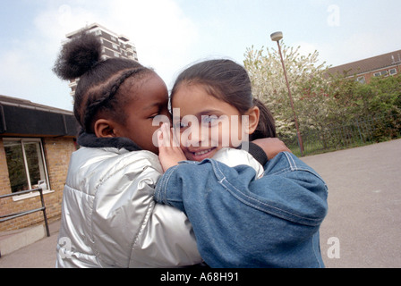 Two girls whispering a secret to each other at break time in primary school. Stock Photo