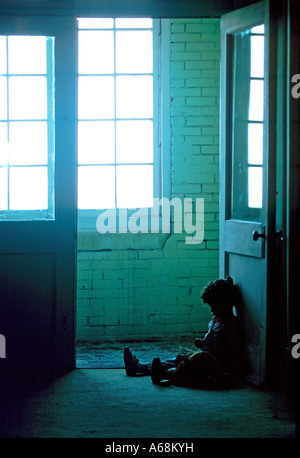 Small child sits alone in the dark dirty hallway of a rundown apartment building Stock Photo