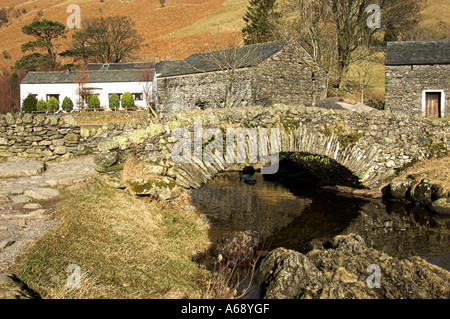 Pack horse bridge over the Watendlath Beck with farm buildings in background.  Watendlath. Stock Photo