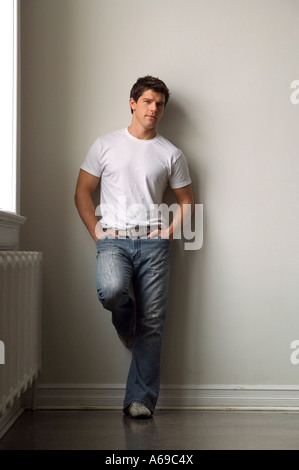 Young adult man leaning against white wall. Stock Photo