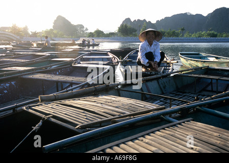 Sunset at Tam Coc, Vietnam. A lady moors her boat on a cluster of rowboats after rowing tourists around on the Ngo Dong River. Stock Photo