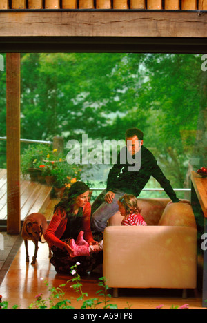 A YOUNG FAMILY IN A MODERN HOUSE WITH LARGE GLASS SLIDING WINDOWS UK Stock Photo