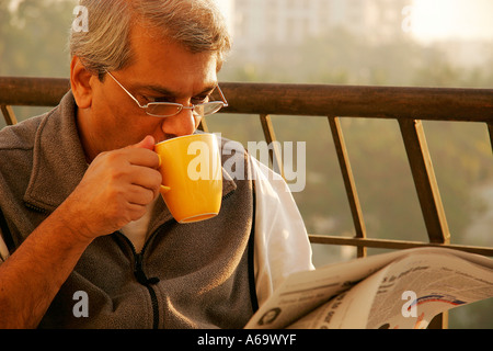 SSK77854 South Asian Indian old senior man drinking tea and reading newspaper sitting in balcony MR#646 Stock Photo
