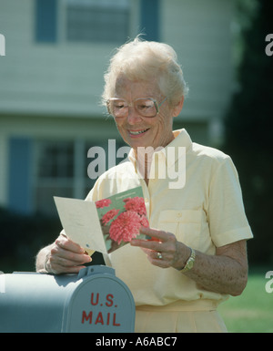 mature woman reading card at mailbox Stock Photo