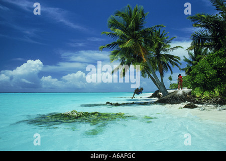 Woman in swing under palm tree and couple embracing on Maayafushi Island in Maldives amid Indian Ocean in North East Ari Atoll Stock Photo
