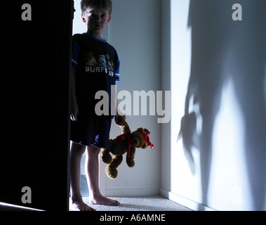 child walking out of the light an pj and carrying his favorite teddy having just got out of bed from nightmare looking for suppo Stock Photo