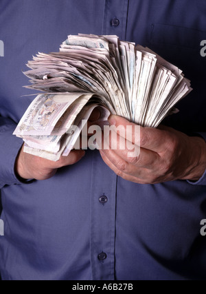 Business man close up two hands gripping hoarding & holding onto stacks of assorted cash in pound sterling money bank notes posed by model England UK Stock Photo