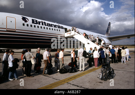 Plane passengers hand luggage queuing to board Britannia jet airliner  to UK 1980s view wheelchair Santo Domingo Airport Dominican Republic Caribbean Stock Photo