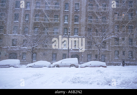 New York City tenement buildings in a snowstorm. Deserted street no traffic or people. A winter blizzard. Parked cars buried in the deep snow drifts. Stock Photo