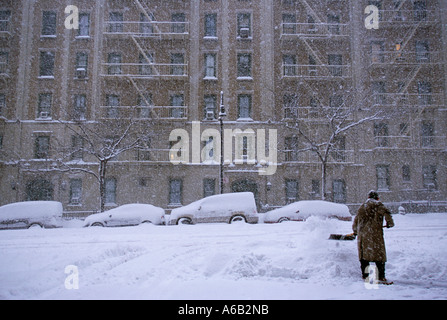 New York City Manhattan tenements. Man shoveling snow during a blizzard. Cars across the street buried in snow. Winter snowstorm in New York. Stock Photo