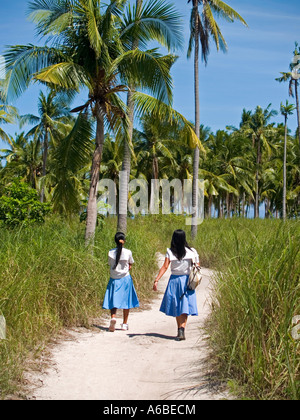 2 schoolgirls walking home under the coconut palms Malapascua Island Philippines Stock Photo