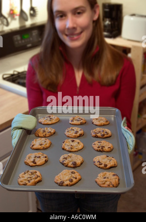 An attractive young woman holds a cookie sheet filled with freshly baked cookies. Stock Photo