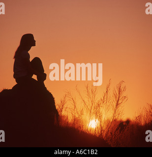 young woman sitting alone on rock at sunset Stock Photo