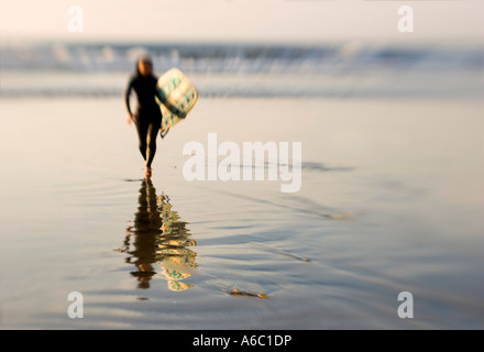 A single female surfer carries her surfboard back to the beach. Stock Photo