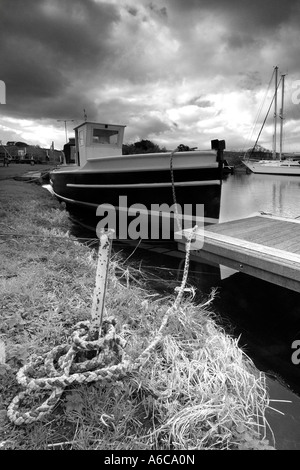 Mono image of a small fishing boat safely moored at Turf Lock on Exeter Ship Canal on a stormy overcast day with heavy cloud Stock Photo