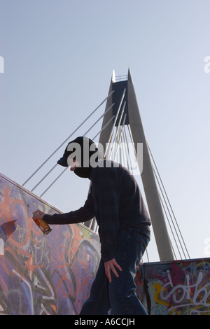 A hooded youth sprays graffiti and marks his tag on a skate-park in Southport Merseyside. Stock Photo