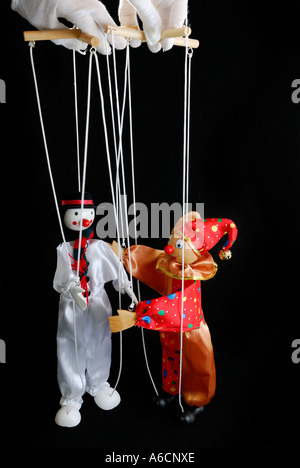 Clown Marionettes about to embrace held by white gloved puppeteer with a black background Stock Photo