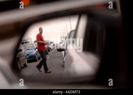 A MAN PICTURED IN A WING MIRROR CROSSING THE MOTORWAY ON FOOT IN A TRAFFIC JAM Stock Photo