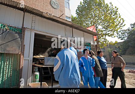 CHINA BEIJING Chinese students gather at storefront restaurant for after school snacks of kabobs grilling in doorway Stock Photo