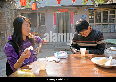 CHINA Chuandixia Chinese couple using cell phones as they share dessert of pummelo Chinese grapefruit in courtyard Stock Photo