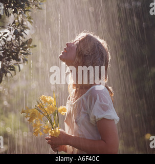 young woman holding flowers enjoying the rain Stock Photo