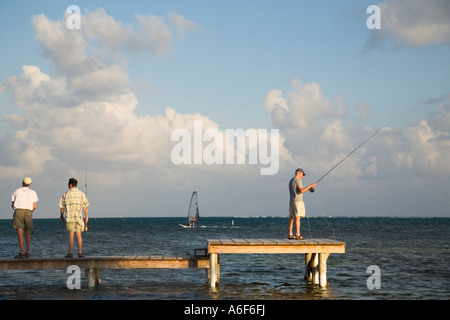 BELIZE Ambergris Caye Three male adults practice fly fishing casting from wooden dock and platform windsurfer in Caribbean Stock Photo