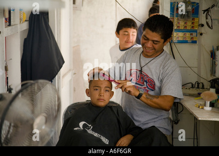 BELIZE Ambergris Caye Man cut male child s hair in small barber shop use pink comb Stock Photo