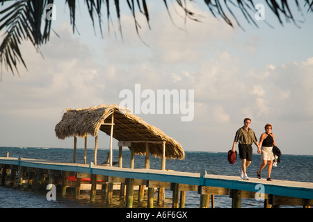 BELIZE Ambergris Caye Couple walk down pier toward restaurant thatched roof on dock structure Caribbean waters Stock Photo