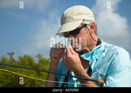 BELIZE Ambergris Caye Adult male fly fishing in flats along shoreline for bonefish change fly on line bite line with teeth Stock Photo