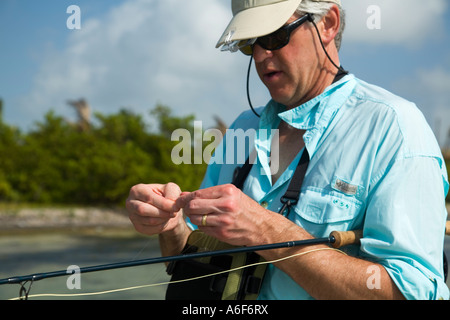 BELIZE Ambergris Caye Adult male fly fishing in flats along shoreline for bonefish change fly on line tie knot Stock Photo